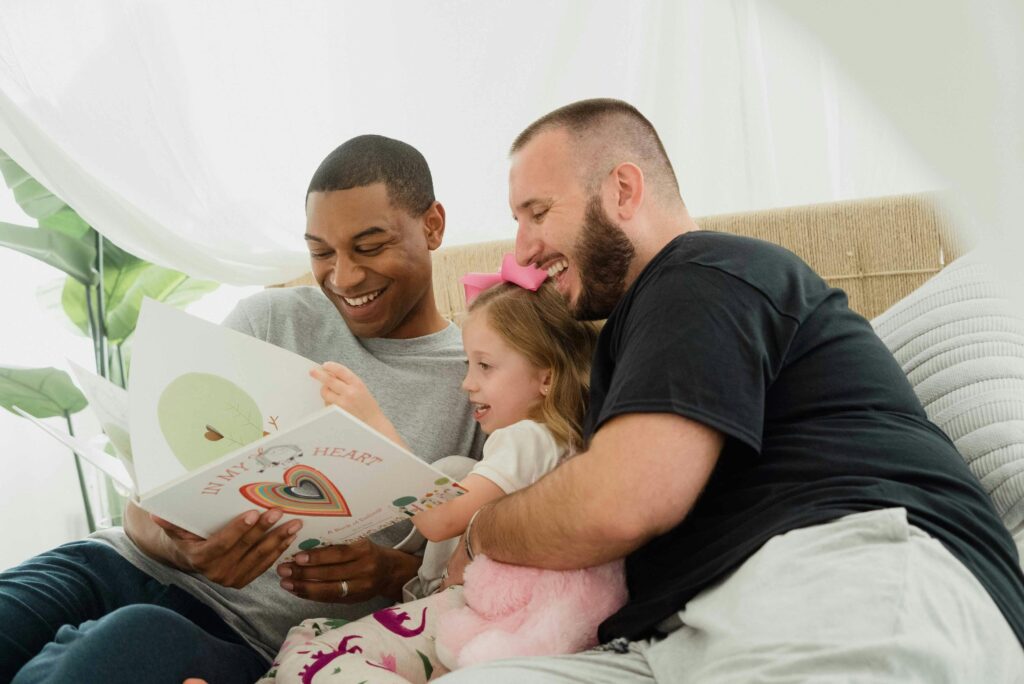 Two fathers and their daughter reading a book